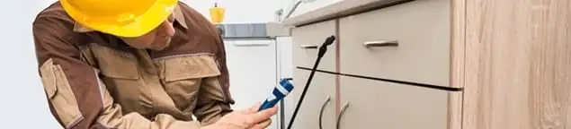 Roach exterminator applying treatment under kitchen cabinets in Bellevue, WA