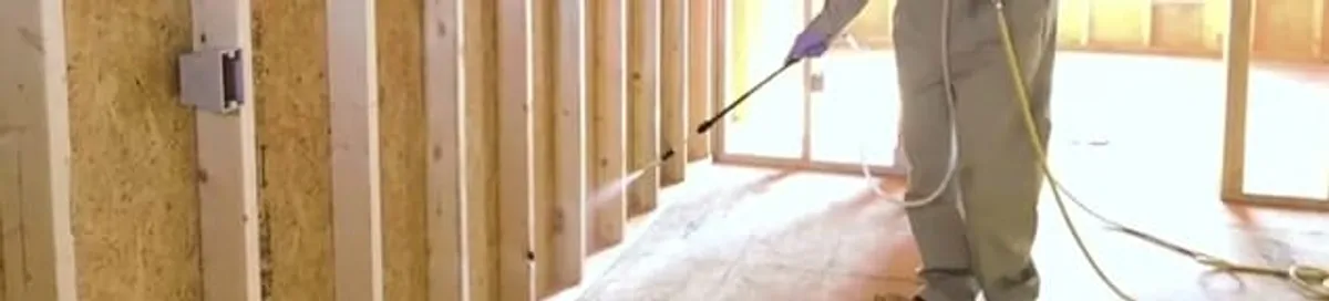 Termite treatment technician applying spray along framing and unfinished walls in Bellevue, WA